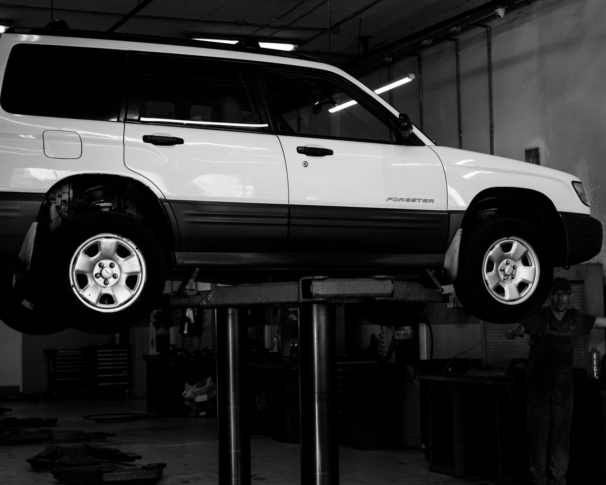 A white SUV raised on a two-post lift inside the shop bay